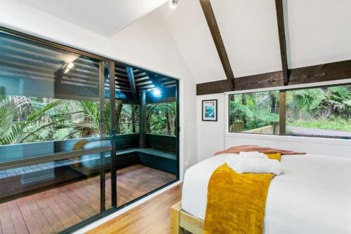 1 dormitorio con 1 cama grande y ventanas grandes en A 1BR slice of Titirangi Heaven - WiFi - Netflix en Auckland