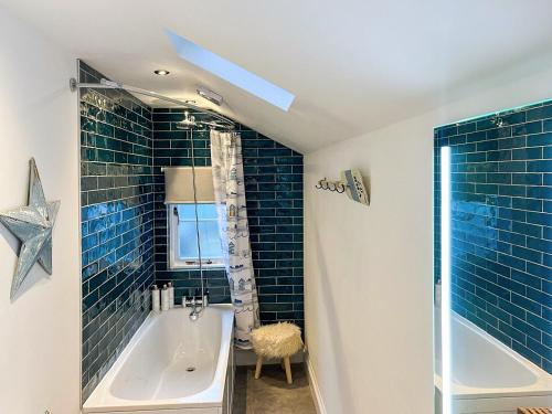 a bathroom with a tub and a shower with blue tiles at April Cottage in Dartmouth