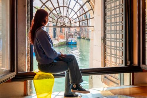 a woman sitting in a window looking out at the water at Casa Flavia ai Morosini - Luxury apartment with Canal View in Venice