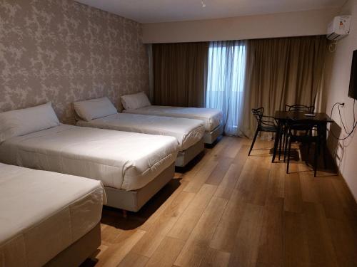 Habitación de hotel con 3 camas y mesa en Avellaneda Aparts & Suites en Buenos Aires