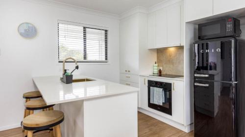 a kitchen with white cabinets and a black refrigerator at Beach Shack Bongaree in Bongaree