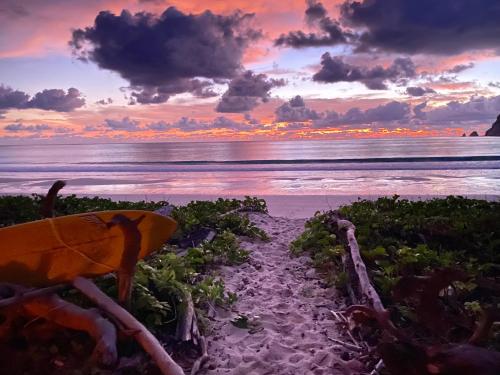 a sunset on a beach with a surfboard on the sand at Camp Tarimbang in Tandulujangga