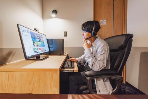 a man sitting in front of a computer with a headset at Relief Kokura ANNEX Book & Stay in Kitakyushu