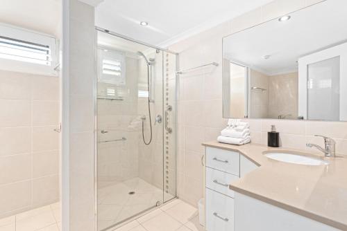 a white bathroom with a shower and a sink at Windward Apartments in Mooloolaba