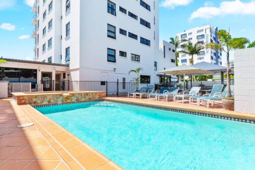 a swimming pool with chairs and a building at Windward Apartments in Mooloolaba