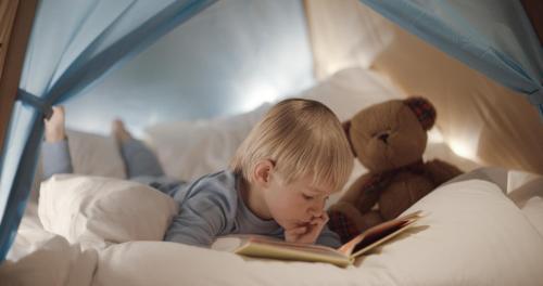 a little boy laying in bed reading a book with a teddy bear at The Ritz-Carlton, Lake Tahoe in Truckee