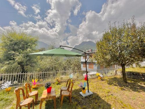 einen Tisch mit Stühlen und einen grünen Sonnenschirm in der Unterkunft Sana cottage - Affordable Luxury Stay in Manali in Manali
