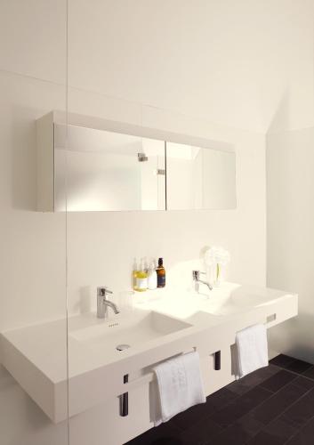 a white bathroom with two sinks and a glass wall at Hotel Post Bezau in Bezau