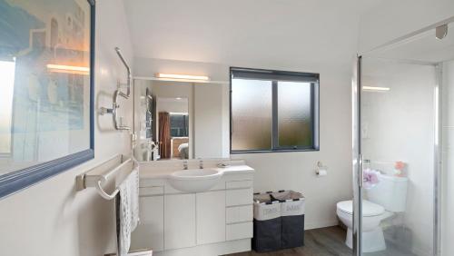 a white bathroom with a sink and a toilet at La Maison Ocean - Mount Maunganui Holiday Home in Mount Maunganui