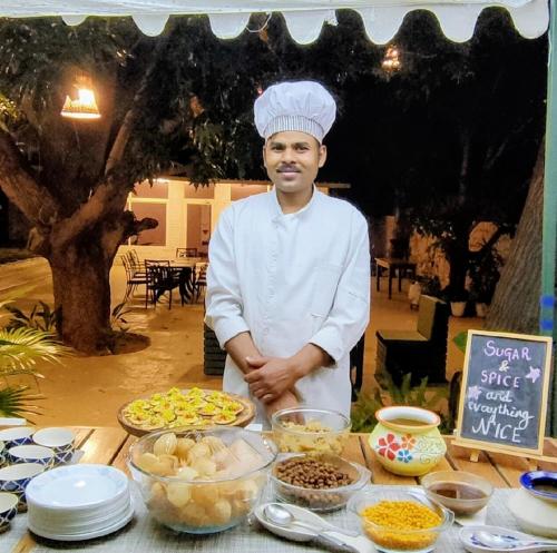 Un chef de pie frente a una mesa de comida. en Vatsalya Vihar - A Luxury Pool Villas Resort, en Udaipur