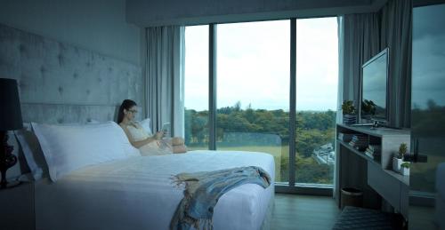 a woman sitting on a bed looking at her cell phone at Pan Pacific Serviced Suites Beach Road, Singapore in Singapore