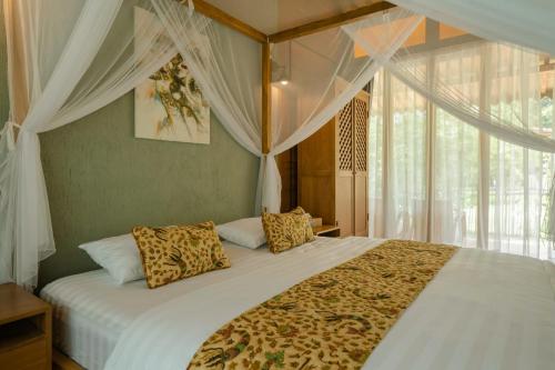 een slaapkamer met een groot bed met witte lakens en gordijnen bij Chandaka Borobudur in Magelang