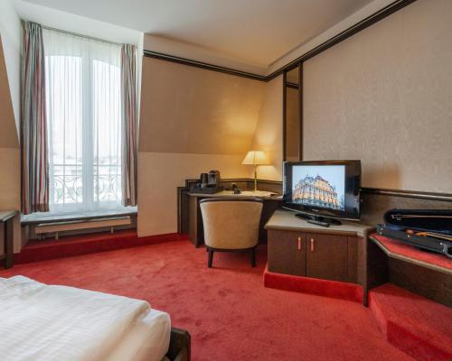 ルツェルンにあるホテル モノポール ルツェルンのベッド、デスク、テレビが備わるホテルルームです。