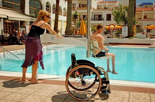 a woman and a man in a wheelchair near a swimming pool at Spa & Sport Hotel Mar y Sol in Arona