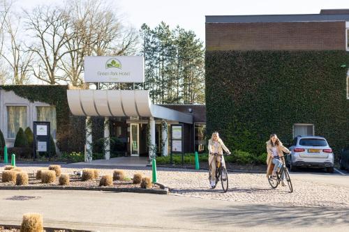two women riding bikes in front of a building at Green Park Hotel Brugge in Bruges