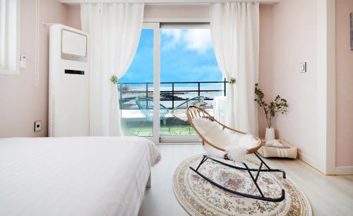 a bedroom with a bed and a chair and a balcony at Pension Haneul Tari in Jeju