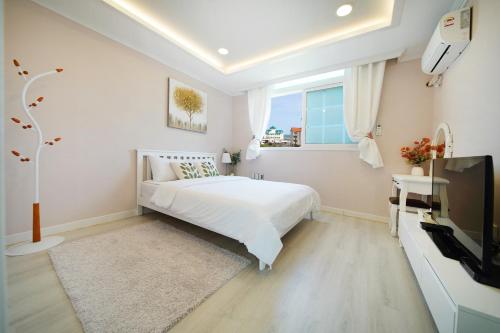 a white bedroom with a bed and a tv at Pension Haneul Tari in Jeju