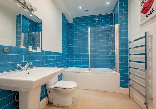 La salle de bains est pourvue de carrelage bleu, d'un lavabo et de toilettes. dans l'établissement Briar Patch, à Southwold