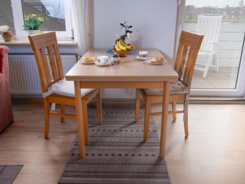 a wooden table with two chairs and a bowl of bananas on it at Apartment Lachmöwe by Interhome in Norddeich