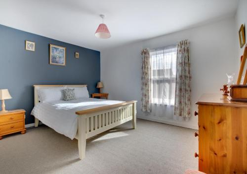 1 dormitorio con paredes azules, 1 cama y ventana en Clyde Cottage en Saxmundham