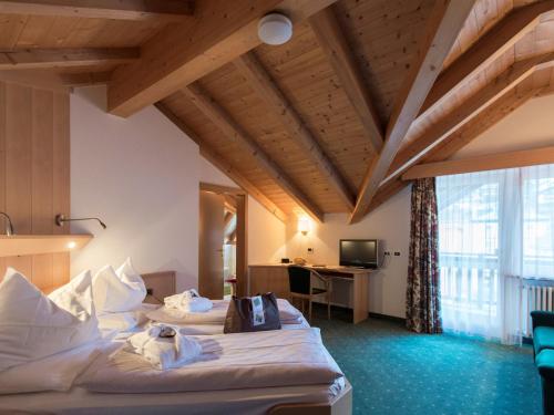 a hotel room with two beds and a desk at Hotel Cosmea in Ortisei