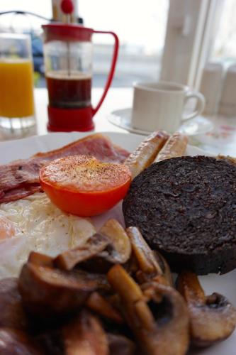 a plate of breakfast food with a sandwich and a tomato at Karrawa Guest House in Kirkwall