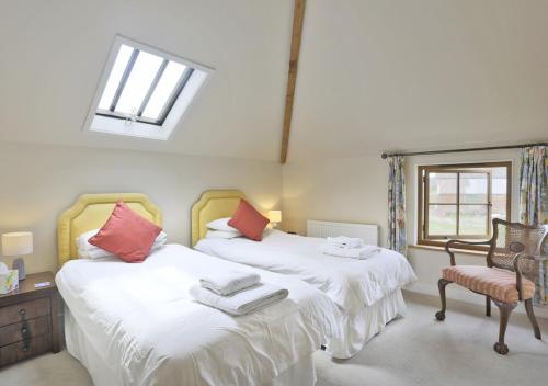 a bedroom with two beds and a window and a chair at Harrow Cottage in Yoxford