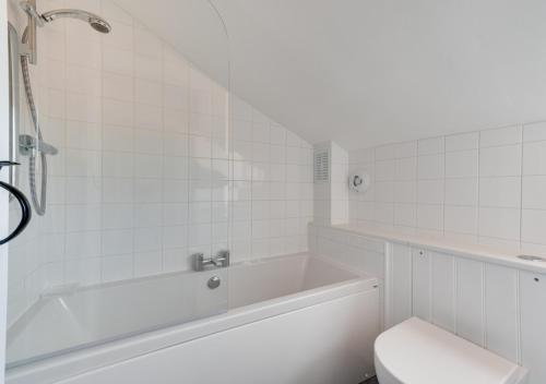 a white bathroom with a tub and a toilet at Japonica Cottage in Wenhaston