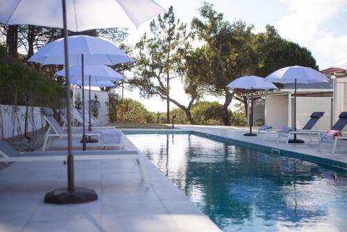 uma piscina com guarda-sóis e cadeiras brancas e uma piscina em À Espera - Turismo Rural,Melides em Melides