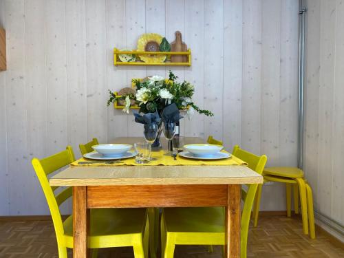 a dining room table with yellow chairs and a vase of flowers at Apartment Della Posta Stambecco by Interhome in Rossa