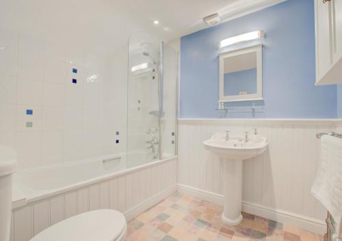 baño blanco con ducha y lavamanos en Sandcastle Cottage, en Southwold