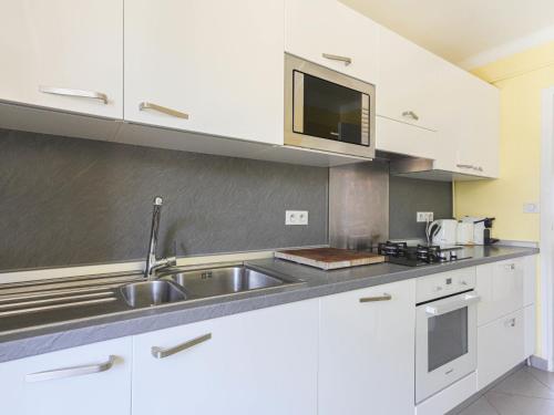 une cuisine avec des armoires blanches, un évier et un micro-ondes dans l'établissement Apartment La plage du Cap by Interhome, à Roquebrune-Cap-Martin