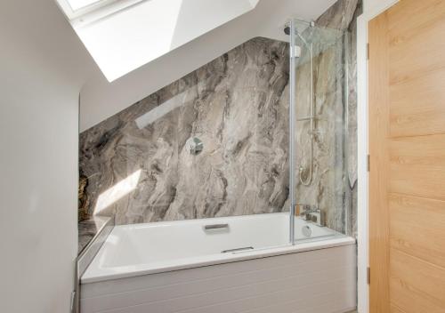 a bathroom with a white tub and a stone wall at The Hatchery in Steeple Bumpstead