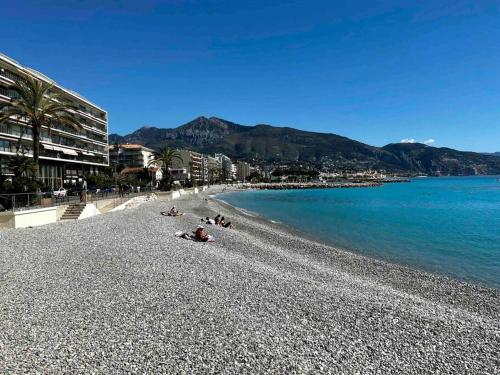 a group of people laying on a beach next to the water at Walk to Beach T2 Climatisé, Vue mer, Parking Privé in Roquebrune-Cap-Martin