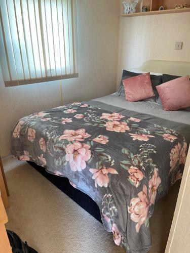 ein Bett mit einer Decke mit rosa Blumen drauf in der Unterkunft Yellow 3 Caravan Ingoldmells 6 berth 3 bedrooms in Skegness