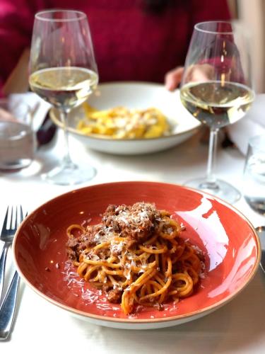 a red plate of pasta on a table with wine glasses at Locanda Da Lino in Pieve di Soligo