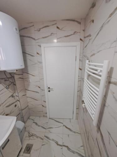 La salle de bains est pourvue d'une porte blanche et de murs en marbre. dans l'établissement Apartmani Swiss LUX Pozarevac, à Požarevac