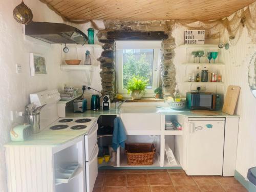 una pequeña cocina con armarios blancos y una ventana en The Old Boathouse at Bunbeg Harbour, en Bunbeg