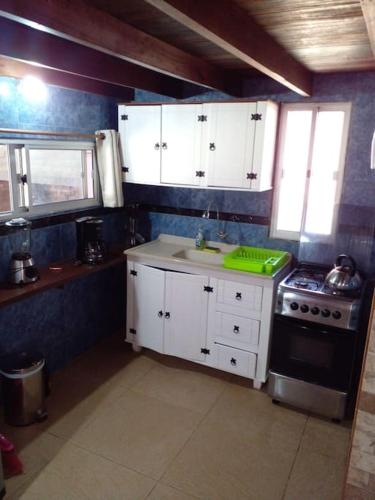 cocina con armarios blancos, fregadero y fogones en Cabañas Punta Palmar (Casa 3) en Punta del Diablo