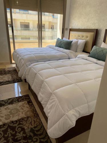 two large beds in a room with a large window at Marina Saidia Luxury Apartment with Pool & Garden View,Residence Tamaris in Saidia 