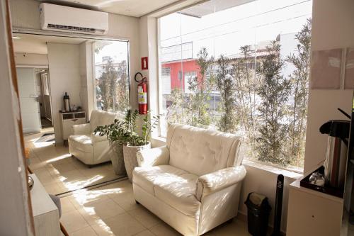 a living room with two white chairs and a large window at Hotel Recanto do Sossego in Uberlândia