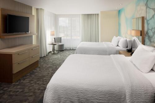 a hotel room with two beds and a flat screen tv at Courtyard by Marriott Detroit Farmington in Farmington Hills