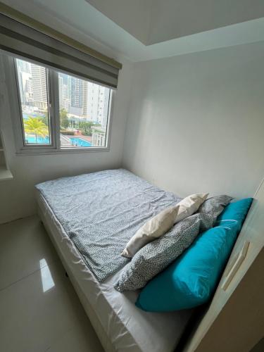 een slaapkamer met een bed met blauwe kussens en een raam bij JC Condo, Jazz Bel-air Makati, POOL VIEW in Manilla