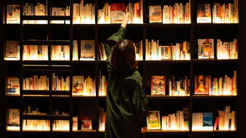 a woman reaching for a book on a book shelf at TUNE STAY KYOTO in Kyoto