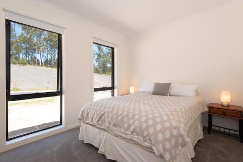 a white bedroom with a bed and two windows at Batemans Bay Delight - Pet Friendly in Batemans Bay