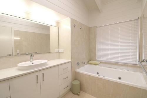 ein Badezimmer mit einem Waschbecken, einer Badewanne und einem Spiegel in der Unterkunft Beach Haven in Merimbula