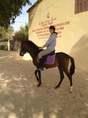 a woman riding a horse in front of a building at Maison Couleur Passion in Nianing