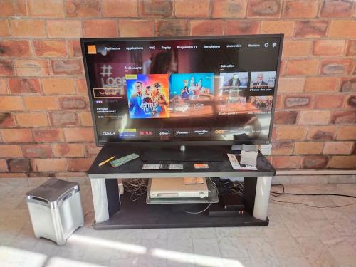 a flat screen tv sitting on a table in front of a brick wall at Gîte La vie au vert Spacieux et autonome in Malay-le-Grand