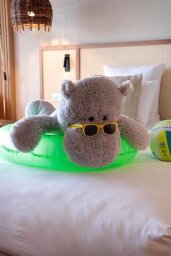 a teddy bear wearing sunglasses sitting on a bed at Golden Tulip Porto-Vecchio in Porto-Vecchio