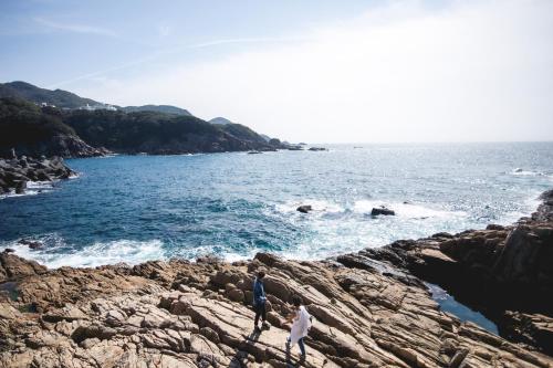 two people walking on the rocks near the ocean at TheMana Village in Tosashimizu
